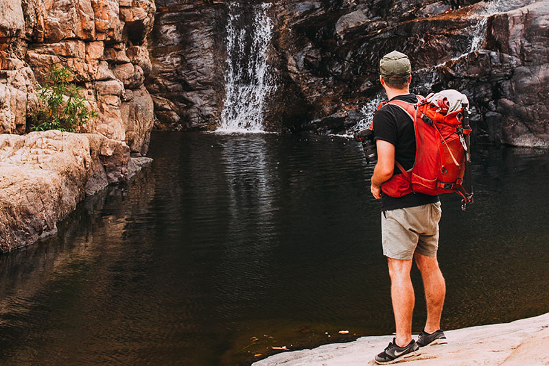Flynlodge traveler with a backpack standing by the stream